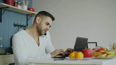 הורה מדבר בטלפון ובודק פרטים במחשב נייד, יושב במטבח